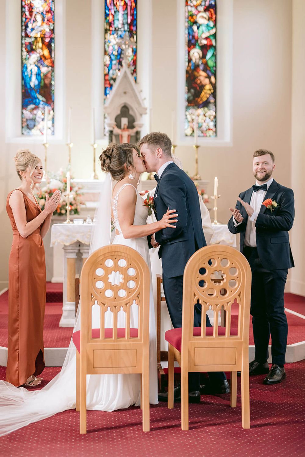 A tender moment captured in a church with stained glass windows as newlyweds share their first kiss.