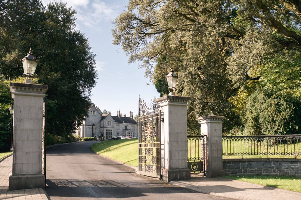 Grand entrance gates with stone pillars leading to an elegant estate driveway lined with trees. Lough Rynn castle