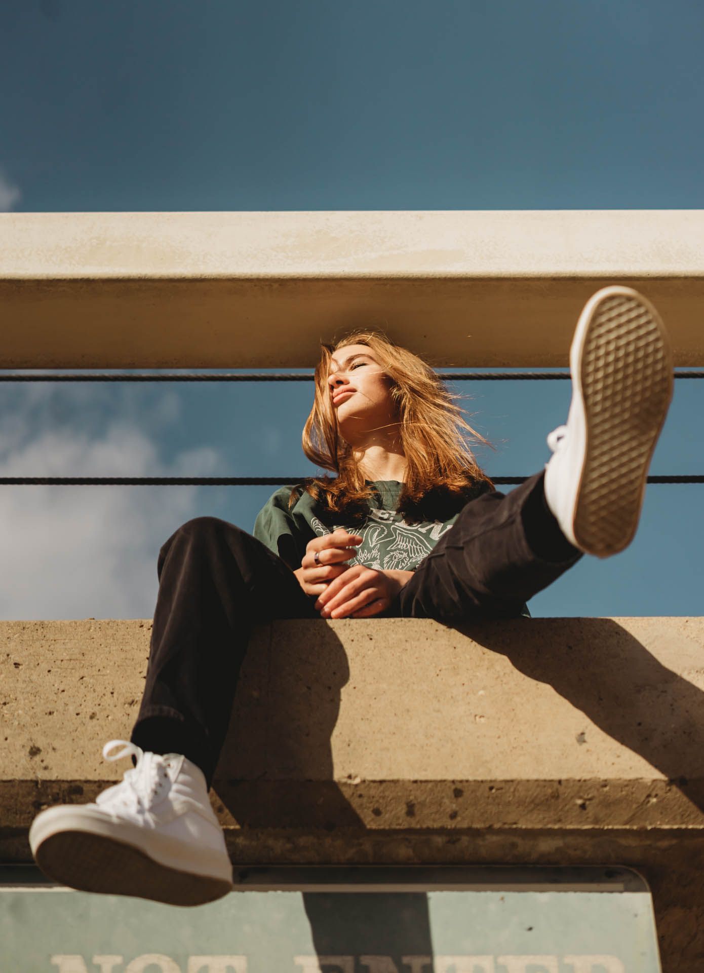 Person lounging on concrete steps in sunlight wearing sneakers and casual clothes.