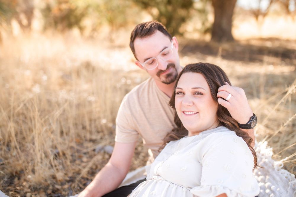 Pregnant woman smiling as husband gently touches her hair in sunny golden grass field.
