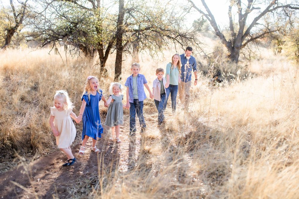 Large family with six children walking together on dirt path through golden dry grass field.
