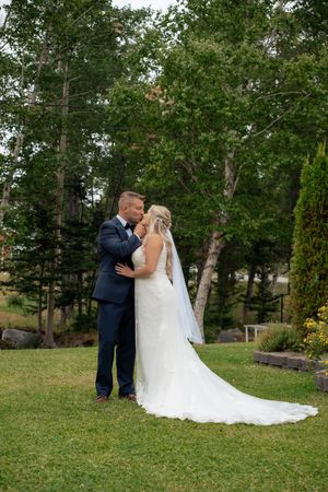 A couple shares a romantic moment on their wedding day in a lush garden setting with birch trees in the background.