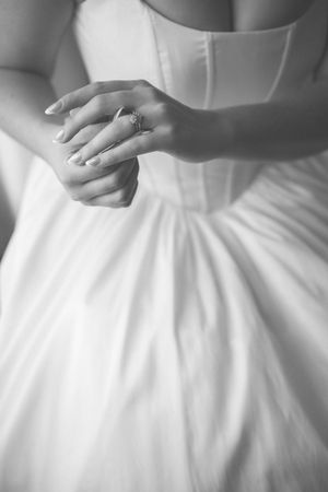 Black and white photo of a bride in a white gown clasping her hands, showcasing an elegant diamond engagement ring.