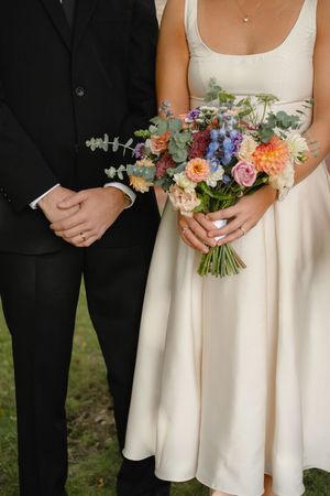 Wedding detail photo showing couple holding colorful spring bouquet with peach, pink and blue flowers against white dress.