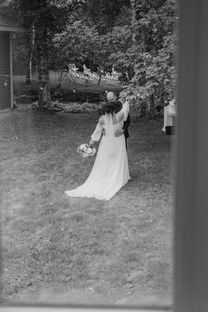 Black and white photo of a bride in a long white dress holding a bouquet while standing in a garden setting.
