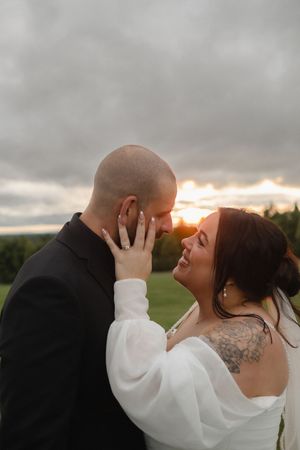 A couple shares an intimate moment at sunset, with the bride wearing a white sweater and the groom in black attire.