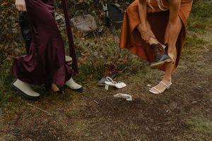 Close-up view of various footwear styles and clothing hems against a natural outdoor ground setting.