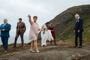 A wedding party stands together on a rugged hillside overlooking a scenic coastal landscape.