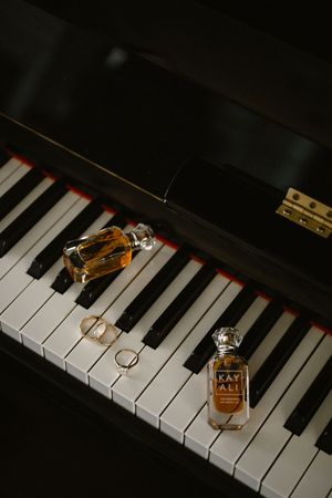 Kayali perfume bottles and gold rings displayed on black and white grand piano keys in elegant flat lay.