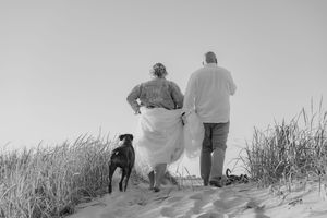 A black and white panoramic sequence shows people walking along a grassy sand dune by the ocean.