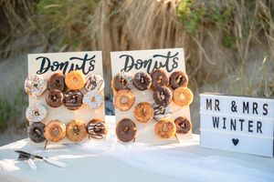 Assorted glazed donuts displayed on a white tiered stand at a wedding reception with signage in the background.
