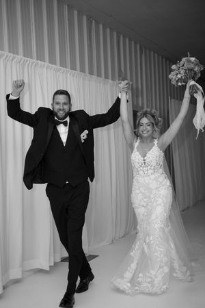 Black and white photo of a joyful bride and groom raising their arms in celebration at their wedding reception.