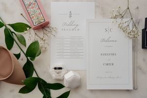 Elegant wedding invitation suite with pink and white accents displayed alongside floral elements and decorative details.