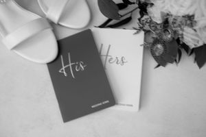 Black and white wedding vow books labeled 'His' and 'Hers' with flowers and ribbon on a light background.
