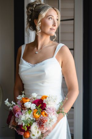 A bride in a classic white wedding dress holds a vibrant bouquet of pink, orange and white flowers.