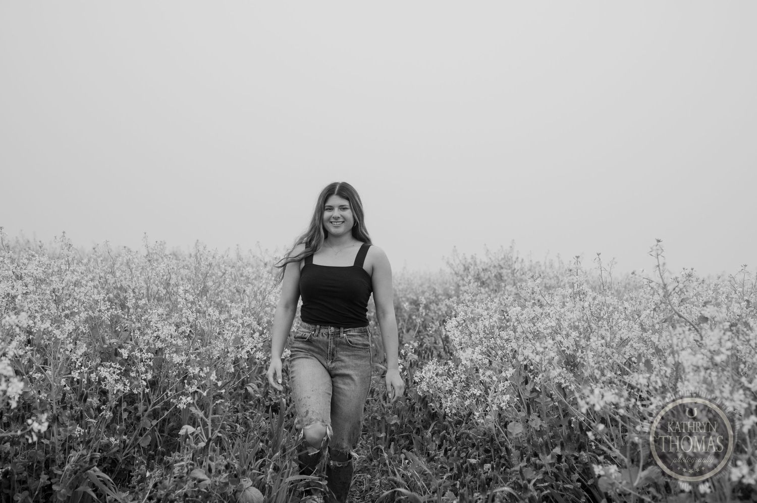 Black and white portrait of someone standing in a flowering meadow under an overcast sky.