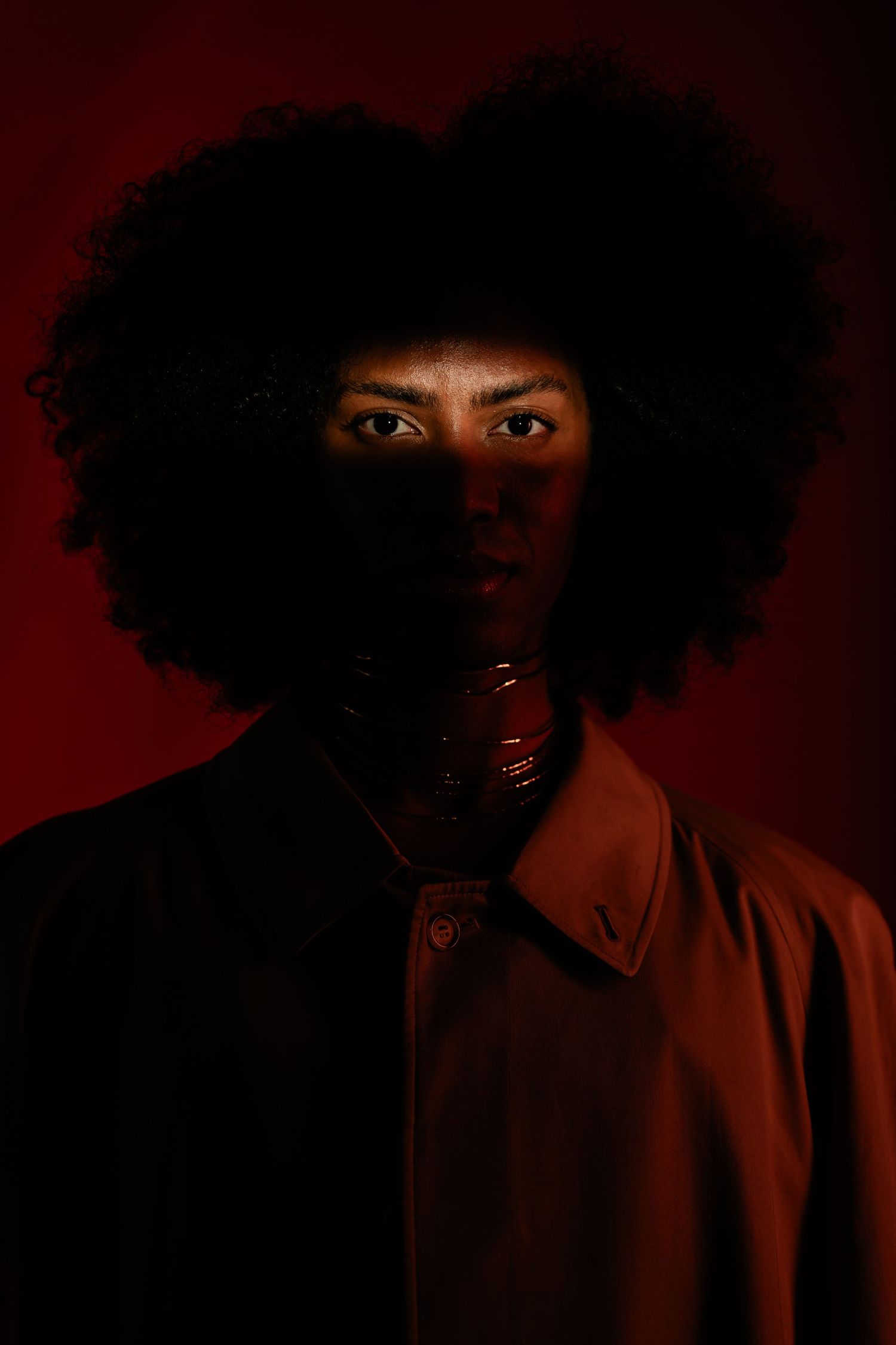 Dramatic portrait against red background featuring natural afro hair and moody lighting.