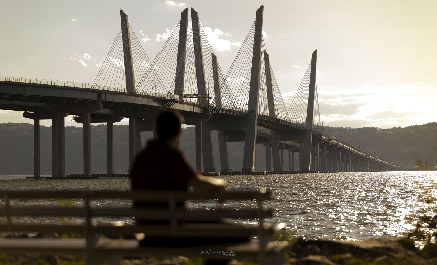 Bridge silhouetted against sparkling water and sunset sky.