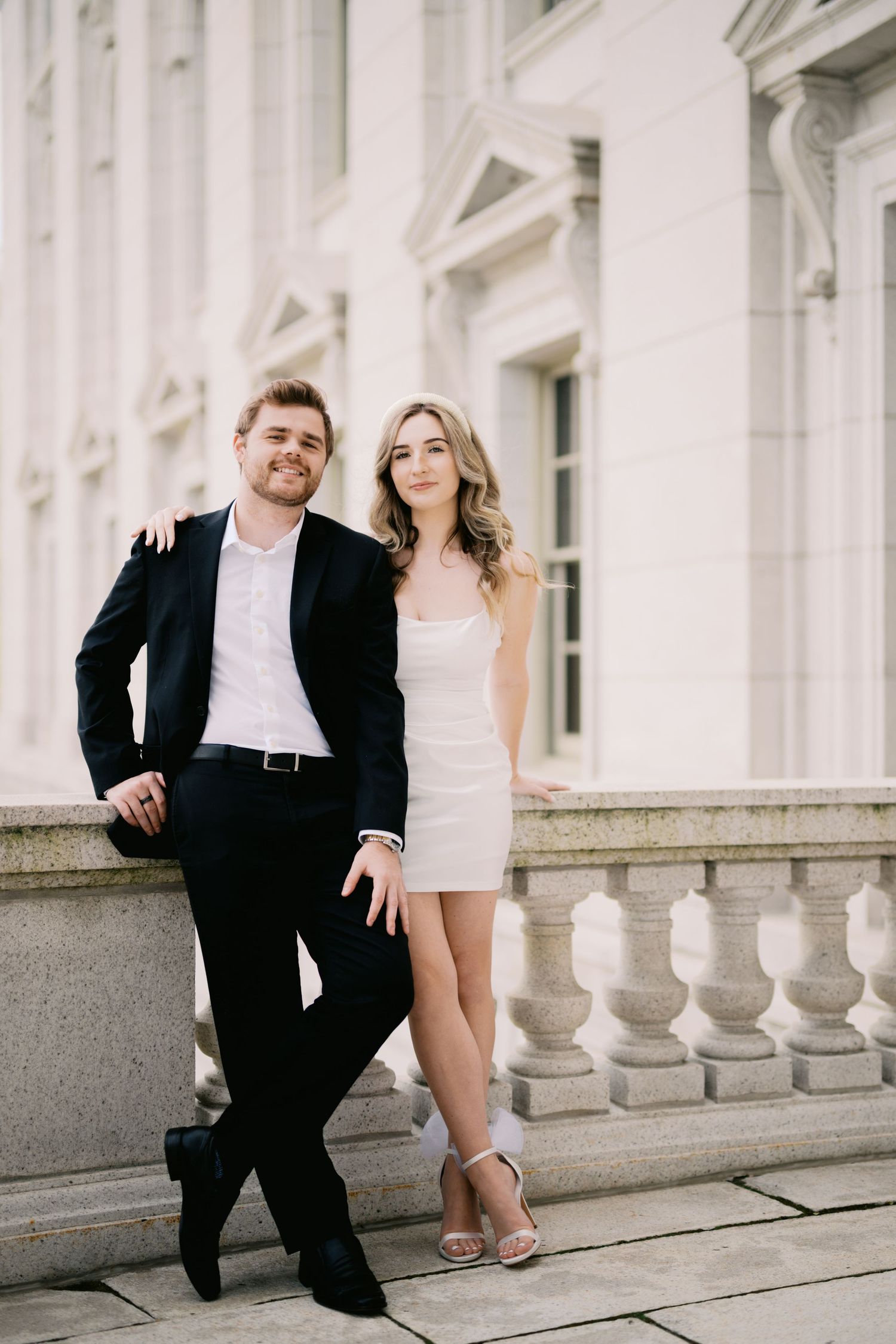 Elegant couple posed at classic white columned building with formal attire and romantic ambiance.