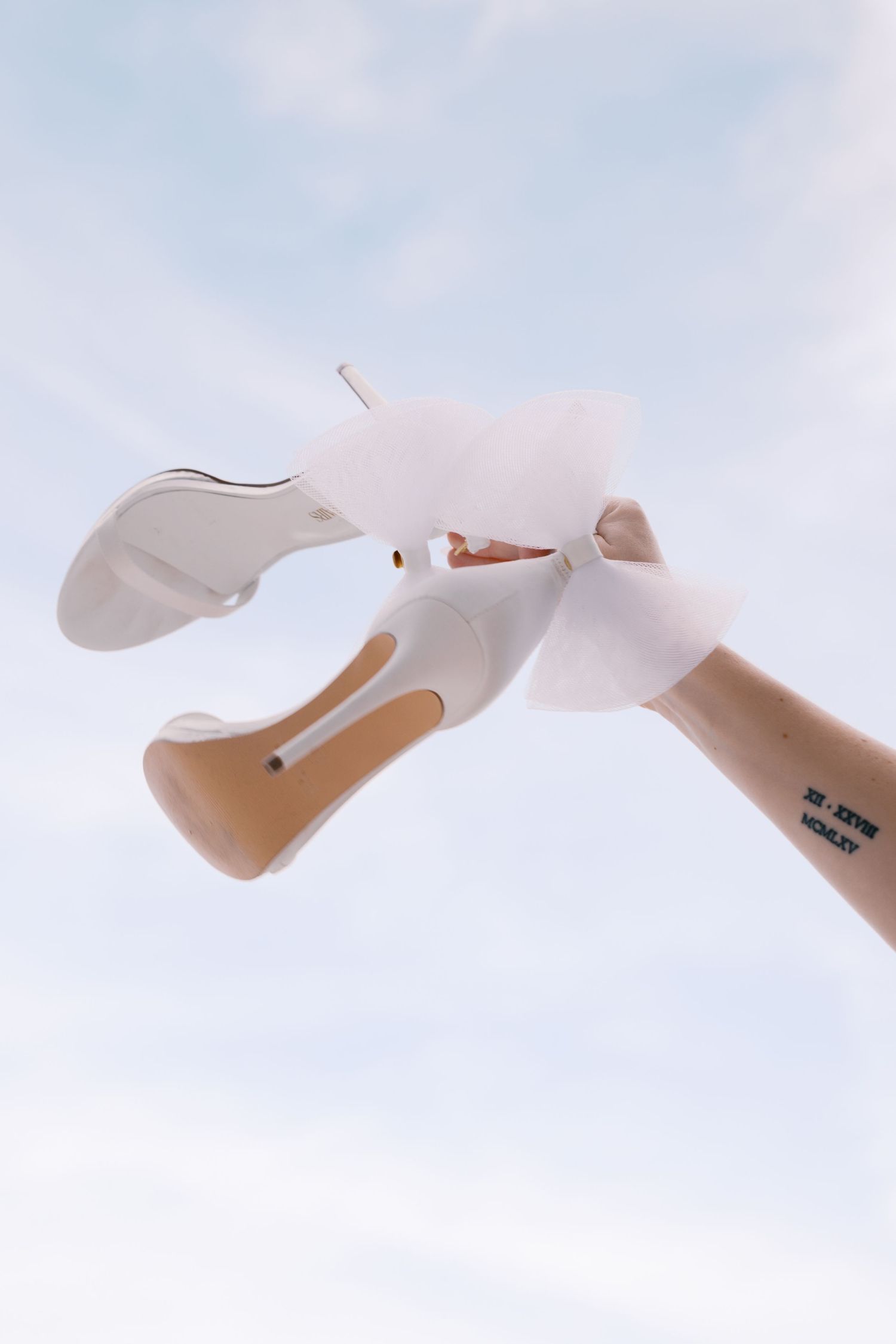 A pair of beige platform high heels floating against a soft blue sky background.
