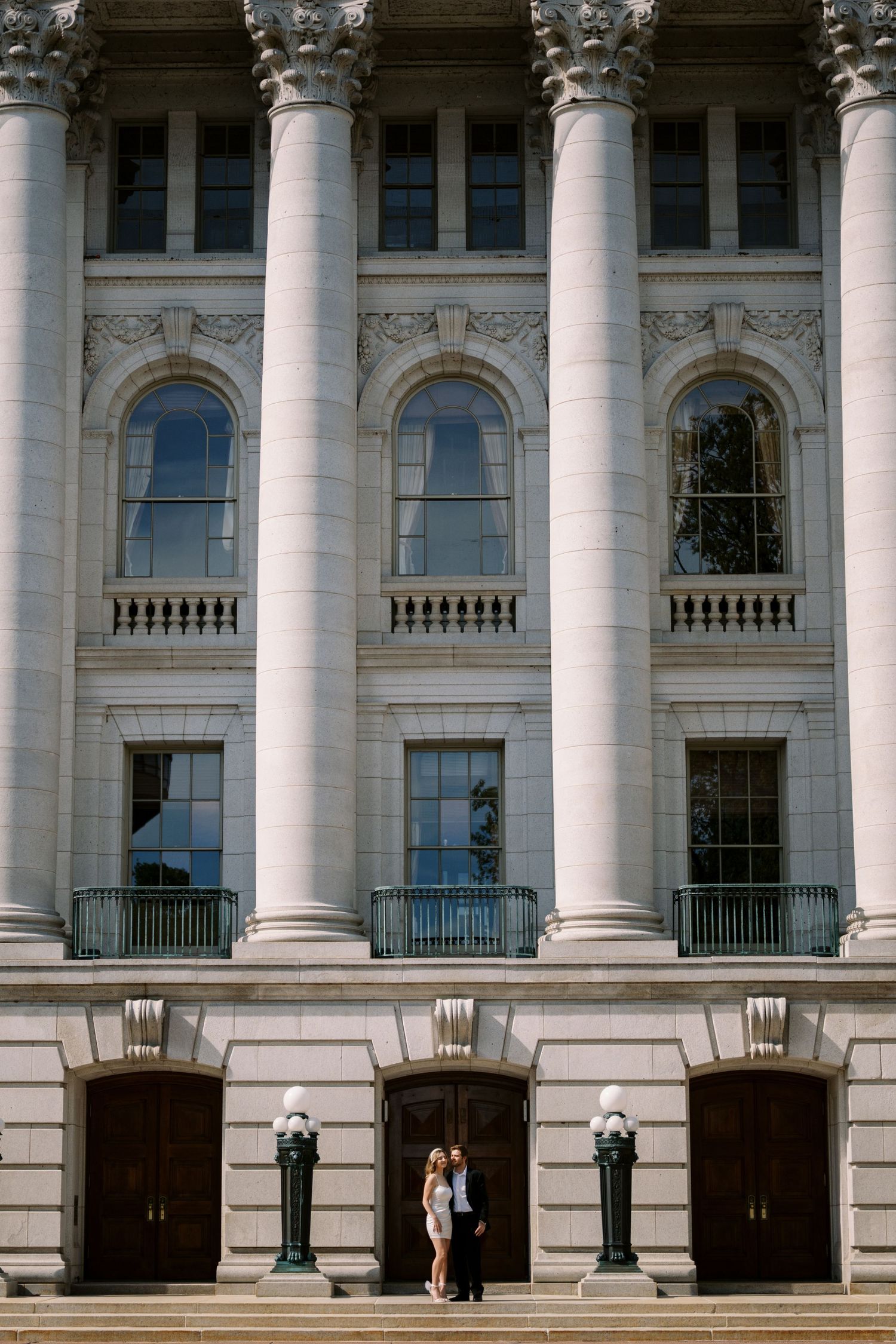 Elegant neoclassical building facade with tall white columns, arched windows, and ornate architectural details viewed from below.