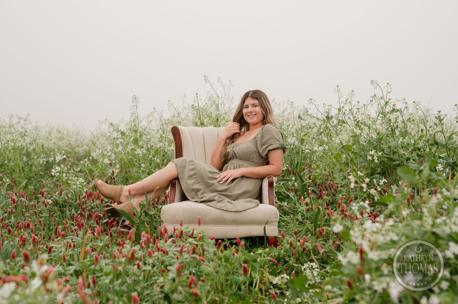 Person relaxes in vintage armchair placed in flowering meadow during outdoor photo session.