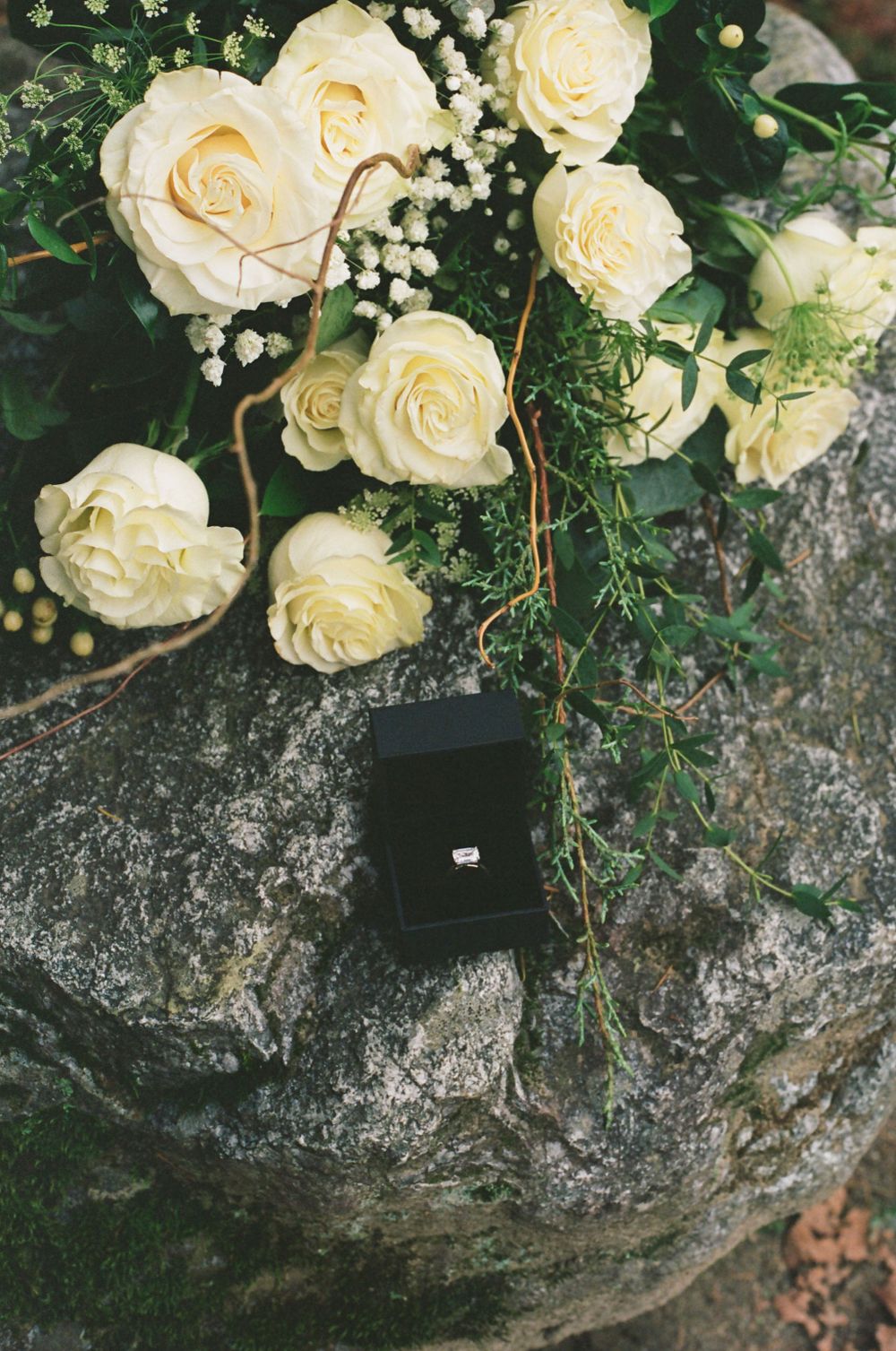 White roses and baby's breath flowers arranged on a natural stone surface.
