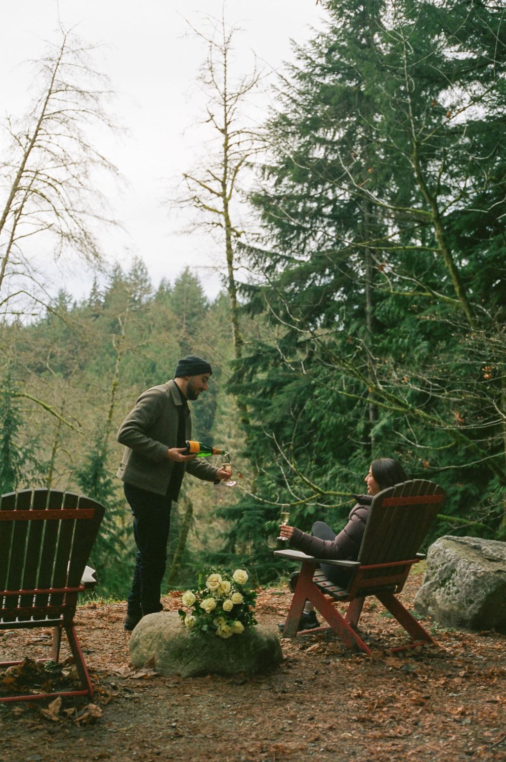 Two Adirondack chairs positioned in a forest clearing with white floral decorations.