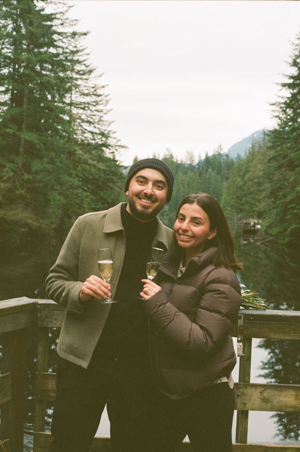 Happy couple sharing drinks and laughter on a deck with mountain views.
