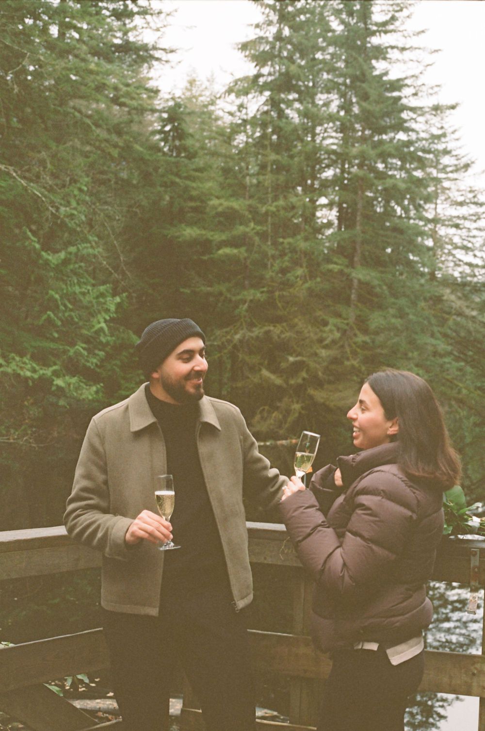 Candid moment between two people laughing and drinking on a lakeside deck.