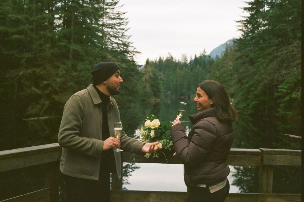 Two people enjoying drinks on a deck overlooking a serene mountain lake.
