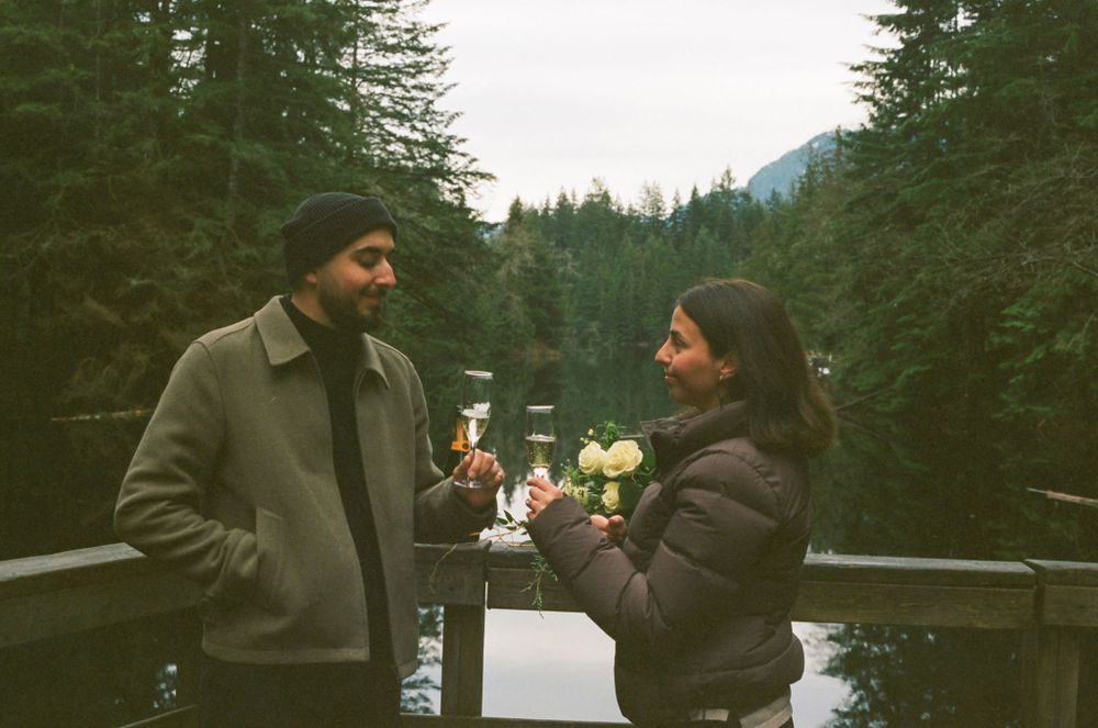 Couple sharing a romantic moment by a lake surrounded by evergreen trees.