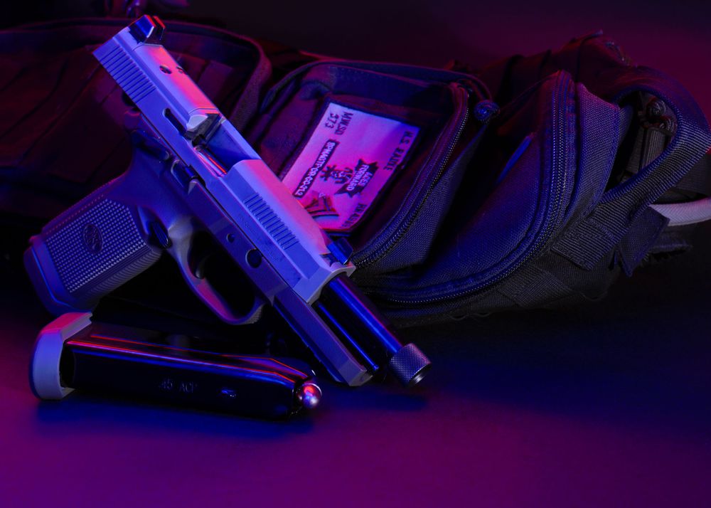Handgun and accessories illuminated with purple and blue lighting on dark surface.