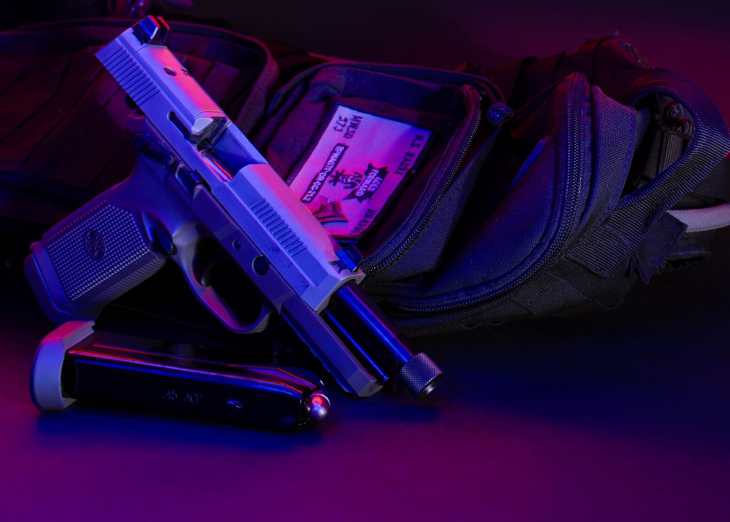 Handgun and accessories illuminated with purple and blue lighting on dark surface.