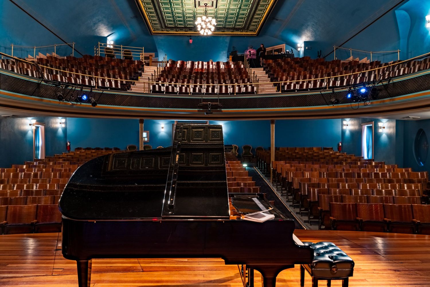 Grand piano on stage in empty concert hall with wooden seats.