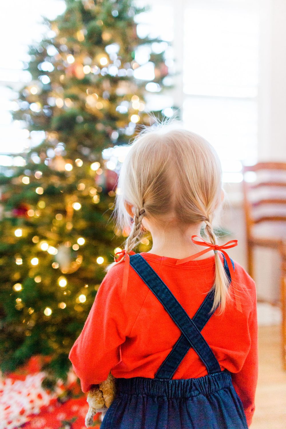 back of little girl in 2 blond braids looking at a christmas tree