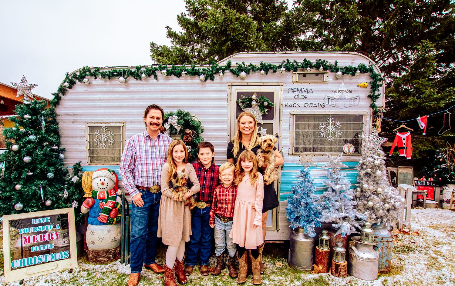 A decorated holiday scene with a vintage camper, Christmas trees, and festive decorations.