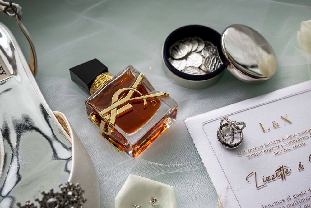 Wedding details featuring YSL perfume bottle and invitation card on a reflective surface.
