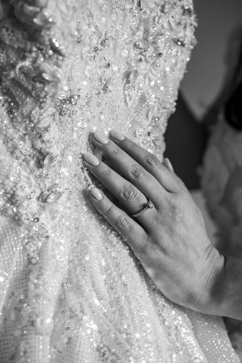 Close-up of hand wearing engagement ring touching sparkly wedding dress fabric.