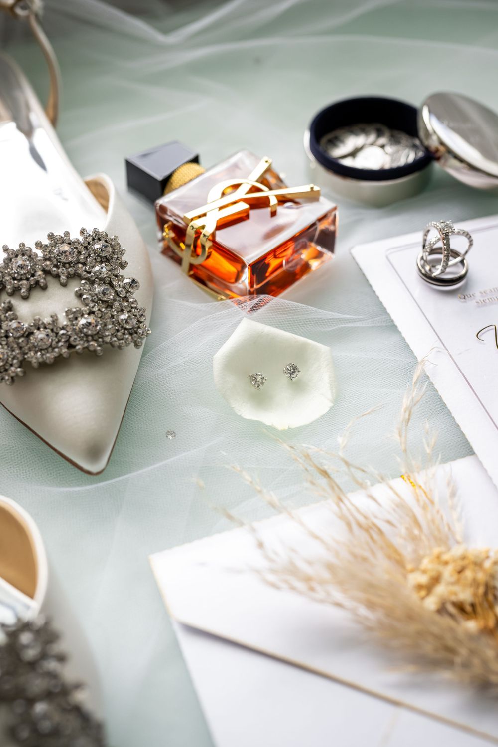 Wedding details flat lay featuring sparkly accessories and invitation cards on mint background.
