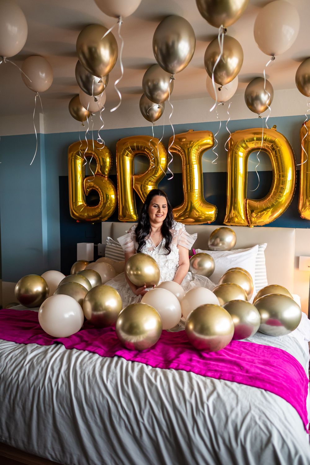 Bride surrounded by gold and white balloons with 'BRIDE' letters on wall.
