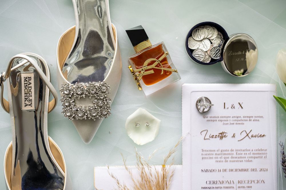 Close-up of wedding invitation and elegant bridal accessories on light blue surface.