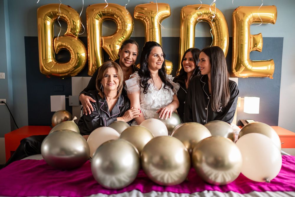 Group celebration with gold 'BRIDE' balloons and festive decorations on bed.