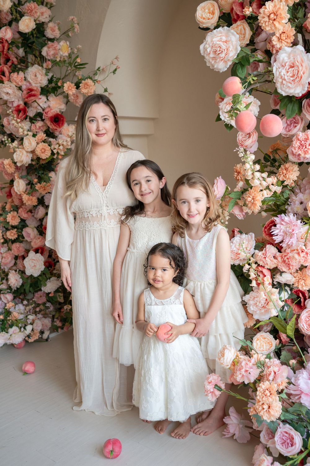 A group portrait under an elegant floral arch with roses in shades of pink and peach.
