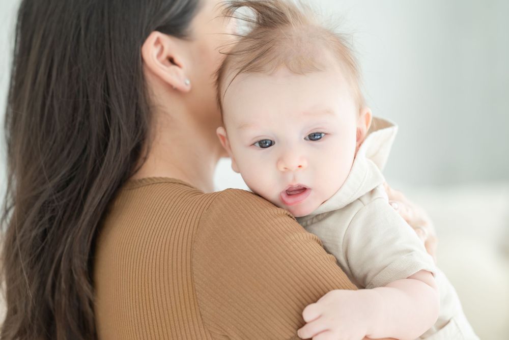 Mother holds baby in tender embrace against bright background.