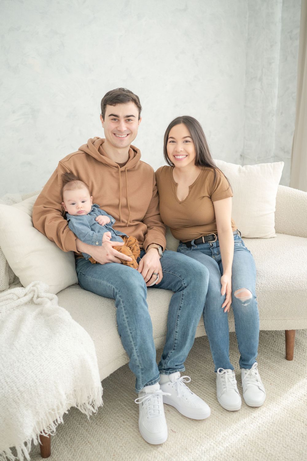 Family of three in matching brown outfits sitting together on white couch.