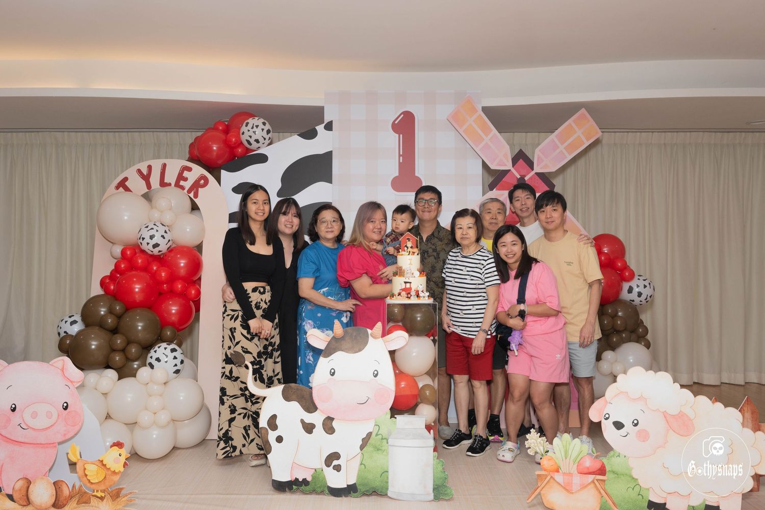 Group photo at a farm-themed first birthday party with balloon decorations and cow print backdrops.