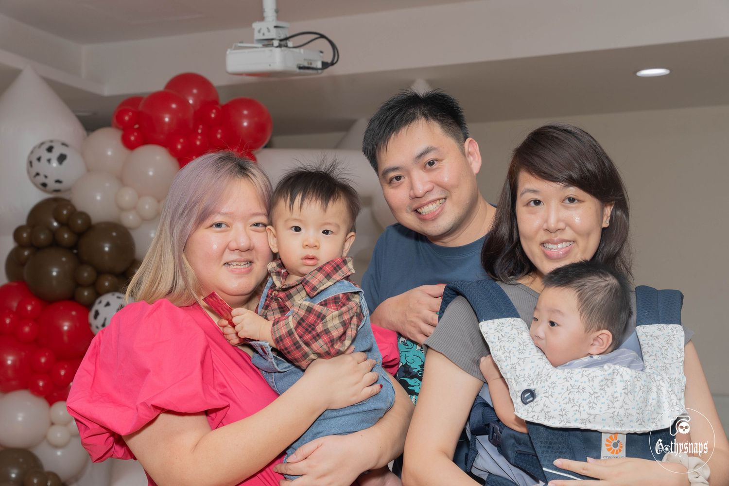 A group photo in front of red and brown balloon decorations at a birthday celebration.
