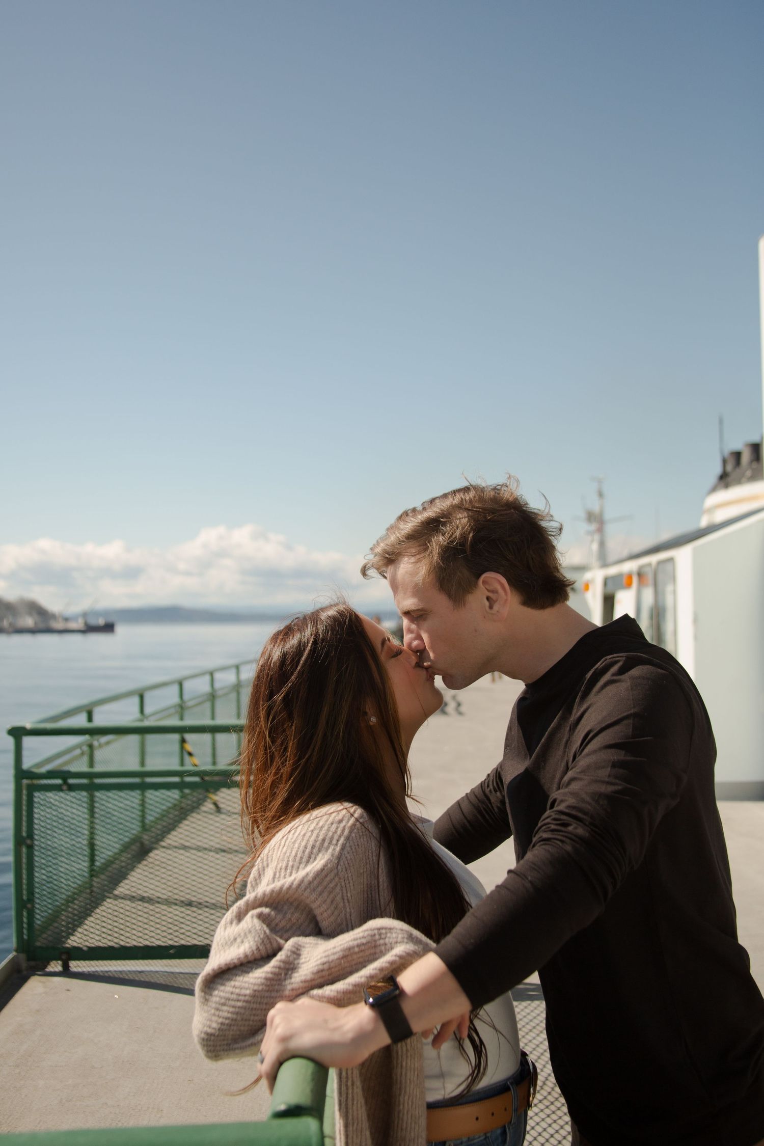 An intimate moment shared between couple on sunny ferry deck with water views.