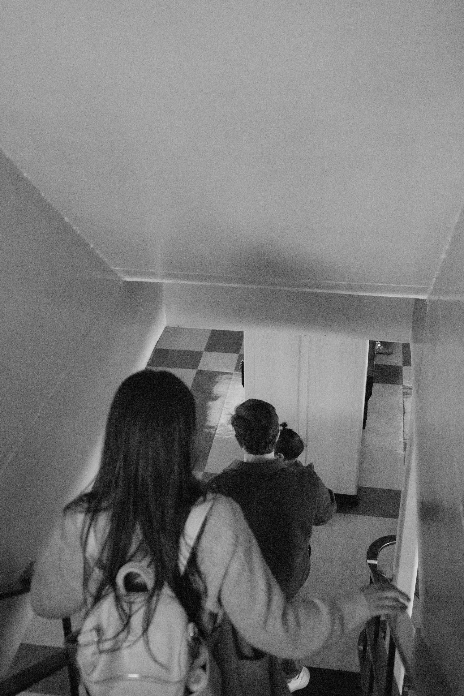 Family ascending stairs in black and white interior hallway shot.